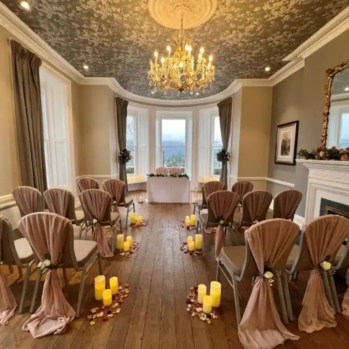 Elegant wedding ceremony room at The Ro Hotel with draped chairs, candles, and floral decor.