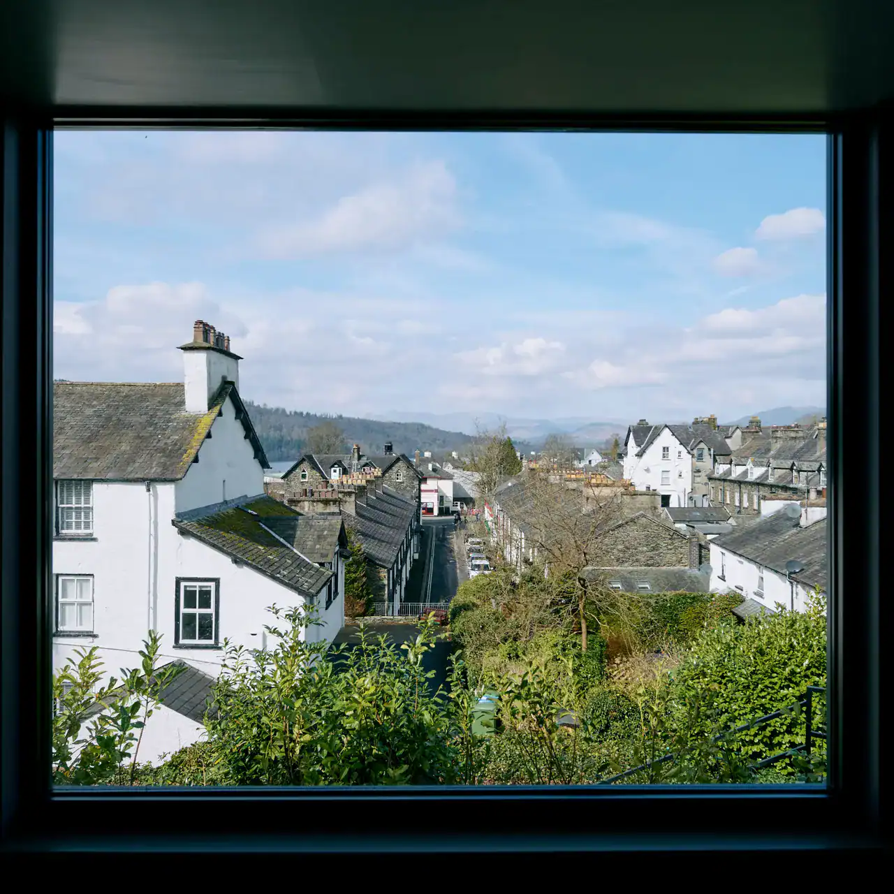 Cozy hotel window view of a charming small town with traditional white houses and scenic hills in the background.