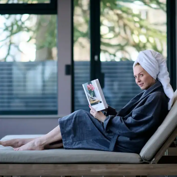 Relaxing guest at The Ro Hotel spa with towel wrap and bathrobe reading a magazine indoors.