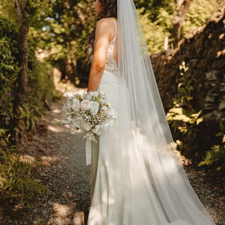 Elegant wedding bride in white dress holding floral bouquet in lush garden setting at The Ro Hotel.