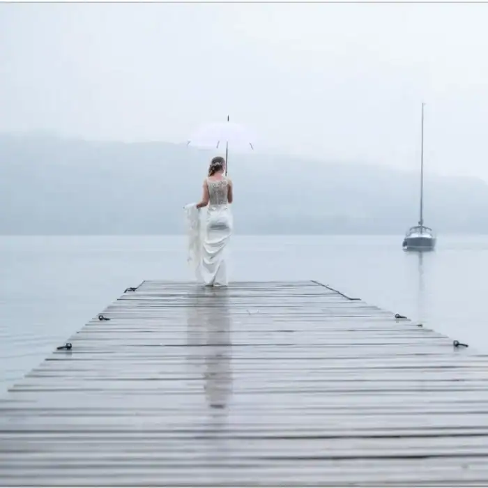 Serene woman walking on a dock with umbrella over calm lake, misty environment, elegant travel getaway.