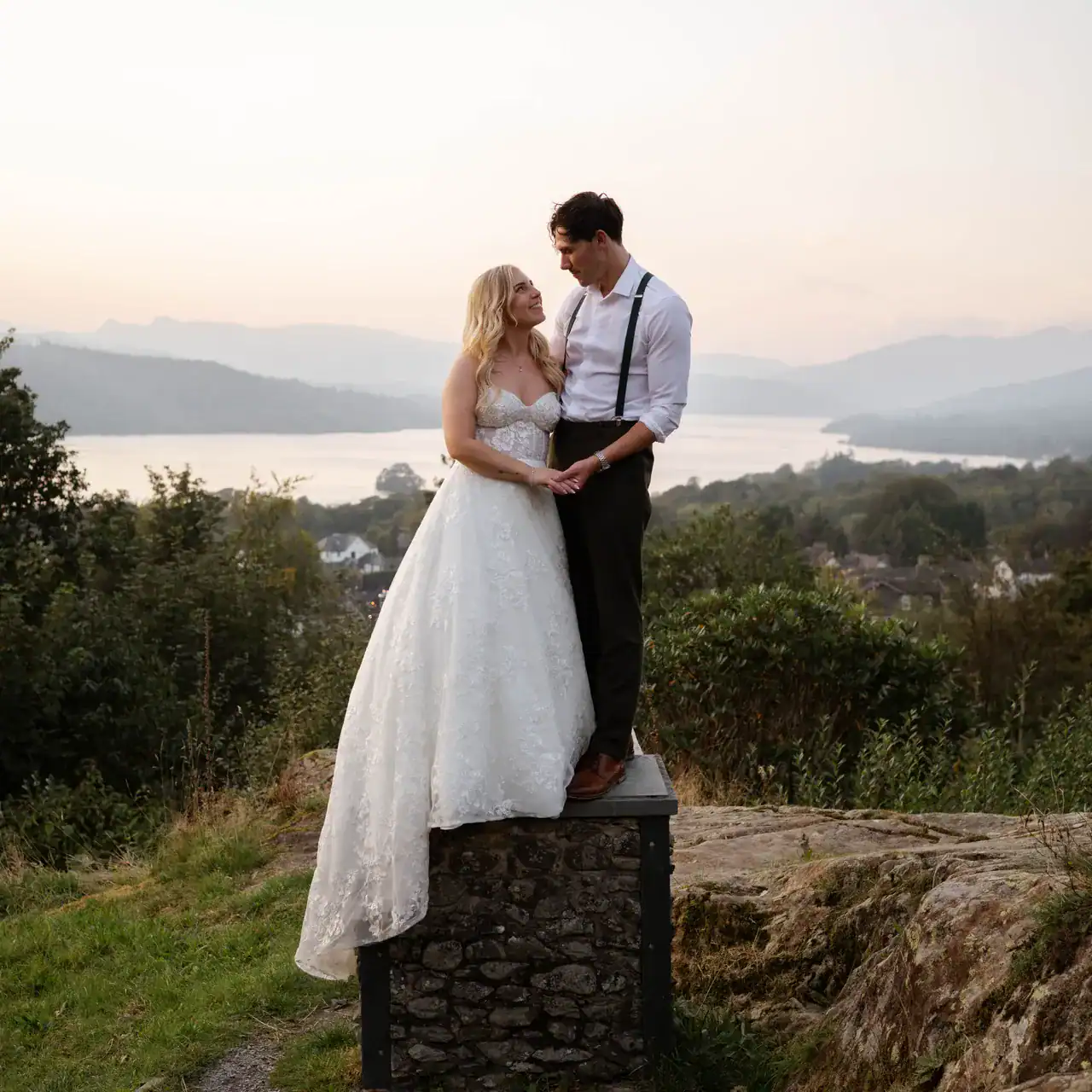 Romantic bride and groom on scenic overlook with lake views and mountains in background.