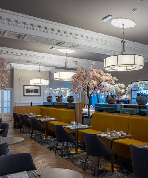 Elegant hotel dining space with modern decor, vibrant yellow seating, floral arrangements, and stylish lighting fixtures.