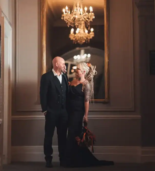 Elegant couple in formal attire at The Ro Hotel lobby with chandelier and mirror, luxurious setting for special occasions.