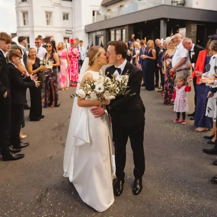 Elegant wedding couple kissing in front of guests outside The Ro Hotel, celebrating love and marriage.