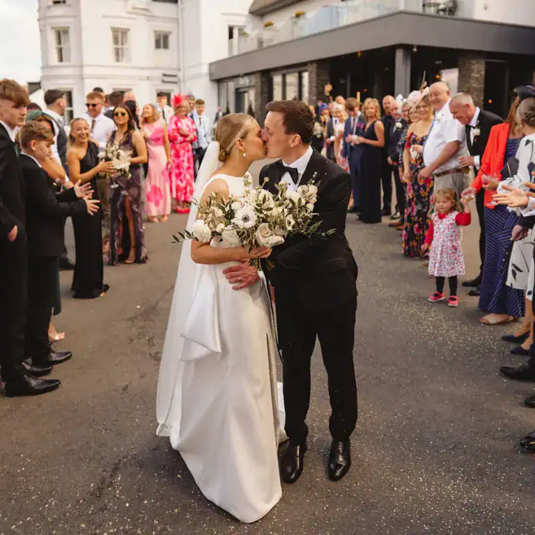 Elegant wedding couple kissing in front of guests outside The Ro Hotel, celebrating love and marriage.