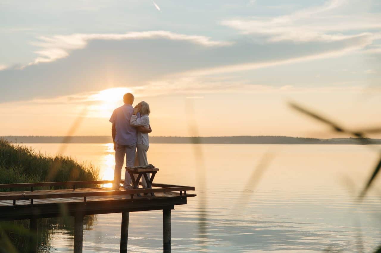 Romantic Break in Lake District The Ro Bowness on Windermere Hotel Older couple stand on a pier overlooking a lake and a sunset
